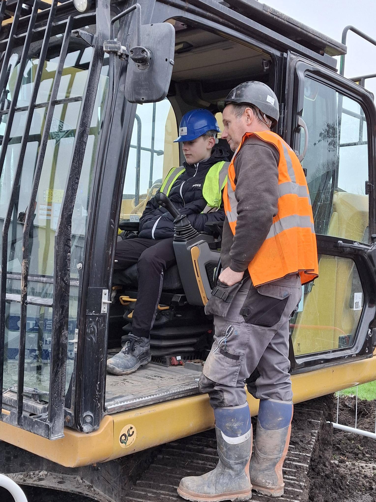 A staff member from Bradley Demolition shows a PVC student the controls at the helm of the digger